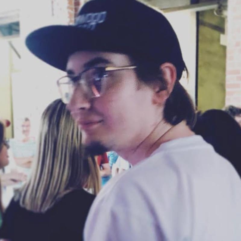 Portrait of a man with brown hair and glasses on a flat gray background.